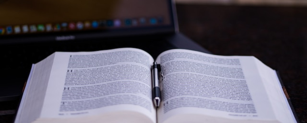 Ein geöffnetes Buch mit einem Kugelschreiber in der Buchmitte liegt vor einem Laptop. Gefunden werden sollen Schlüsselstrategien für die IT-Sicherheit eines Unternehmens.